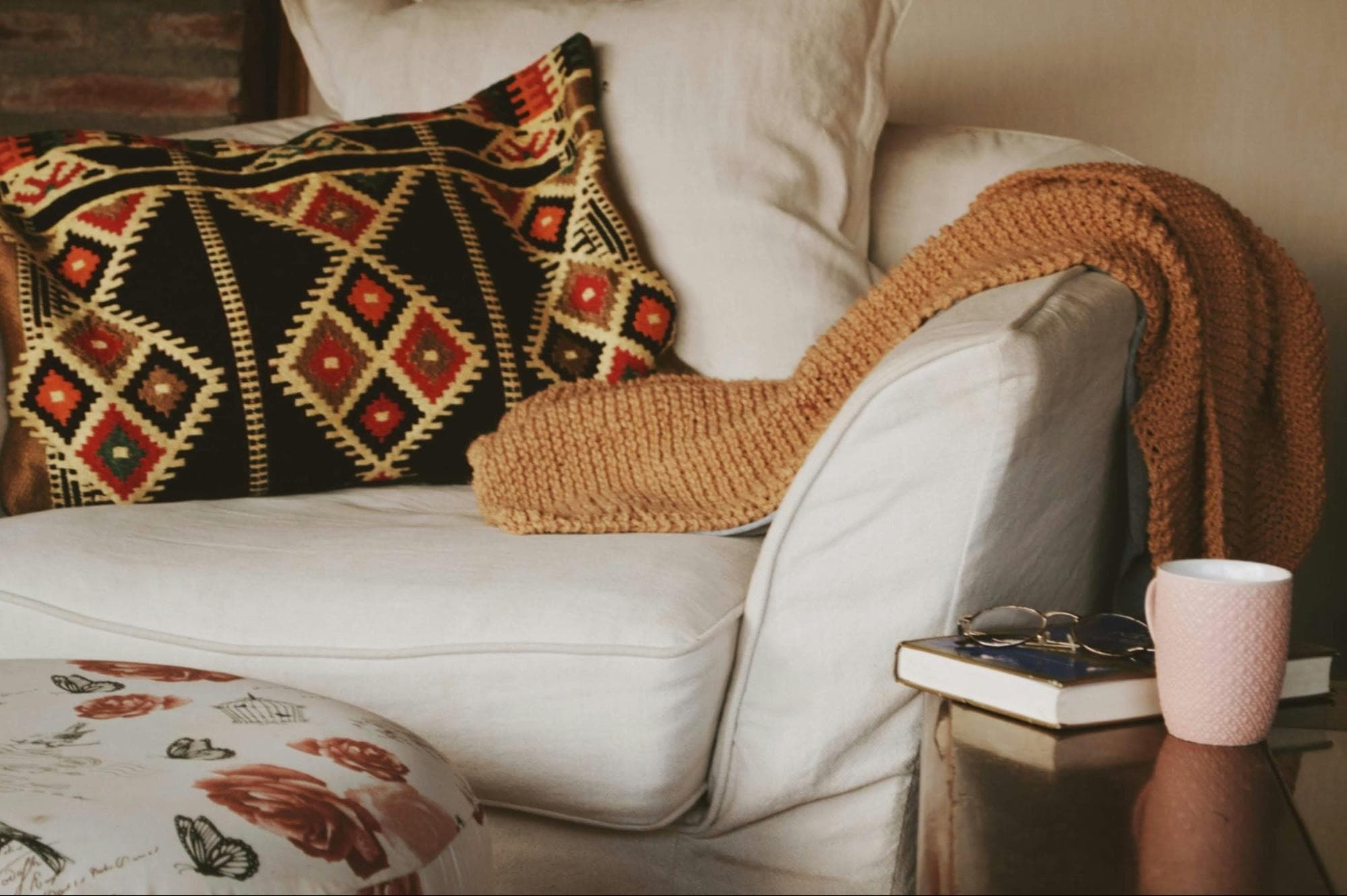 A softly lit couch with a throw, an open book and a mug set down nearby